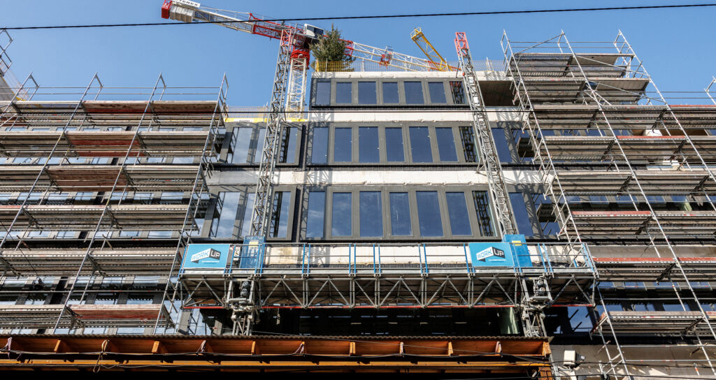 Baustellenfoto der Fassade: Ein Baugerüst steht vor dem Gebäude und ein Kran steht dahinter.