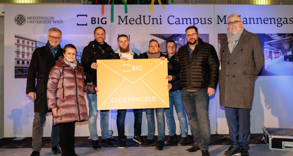 Eine Gruppe an Personen hält einen großen, gelben, bedruckten Karton. Alle lächeln in die Kamera.