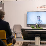 Ein Mann spricht bei einer Konferenz und ist virtuell zugeschalten.