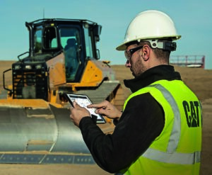 Bauarbeiter steht vor einem Bagger und hält einen Tablett PC in der Hand