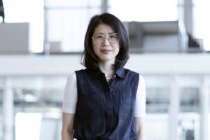A woman wearing a blue and white top with shoulder-length hair smiles gently at the camera.