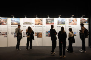Besucher*innen stehen vor einer Wand mit den Projekten und deren Beschreibungen,