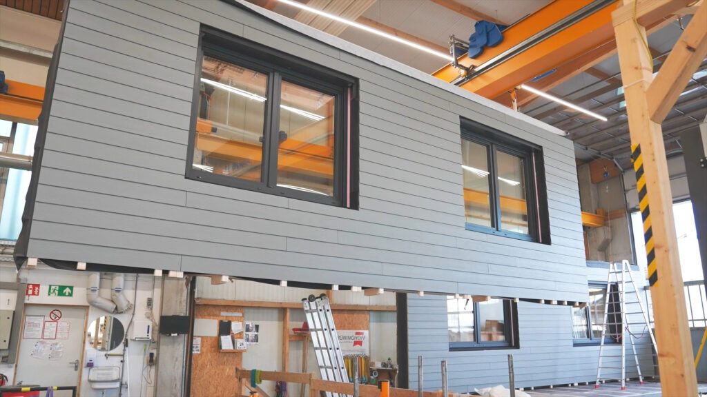 Die Fassadenelemente werden in der Werkshalle vollständig vor-montiert – mit Fenstern, Dämmung und Versorgungstechnik. © Ecoworks
