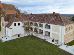 Ein Hof mit hellgelber Fassade steht im Grünen.