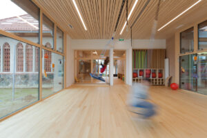 Ein moderner, heller Kindergarten mit vielen Holzelementen und großen Fenstern.