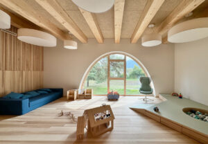 Ein Zimmer in einem Holzhaus. Ein großes, rundes Bogenfenster füllt den hellen Raum mit Licht.