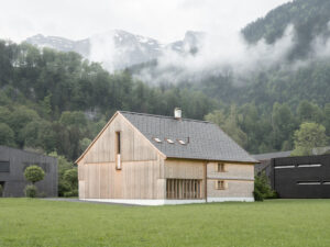 Ein Museum im modernen Holzhütten-Stil. Das Haus steht allein im Grünen, im Hintergrund ein Wald und Wolken. Das Haus ist aus hellem Holz.
