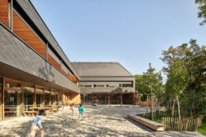 Ein modernes Schulgebäude mit großen Fenstern und viel Holz. Der Außenbereich hat Bäume.