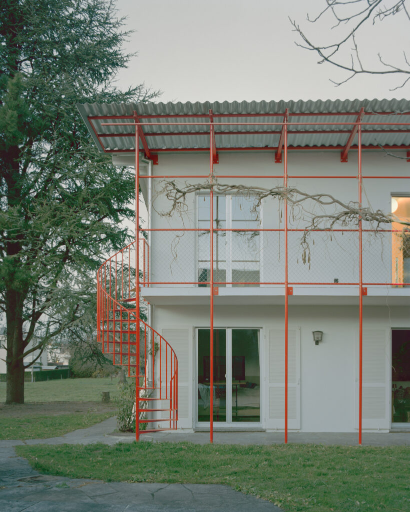 Ein einstöckiges Haus mit roten Akzenten: Geländer und Stufen sind aus rot lackierten Metall.