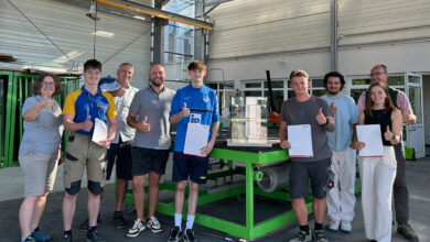 Fünf strahlende, frischgebackene Glasbautechniker*innen mit ihren Prüfer*innen.