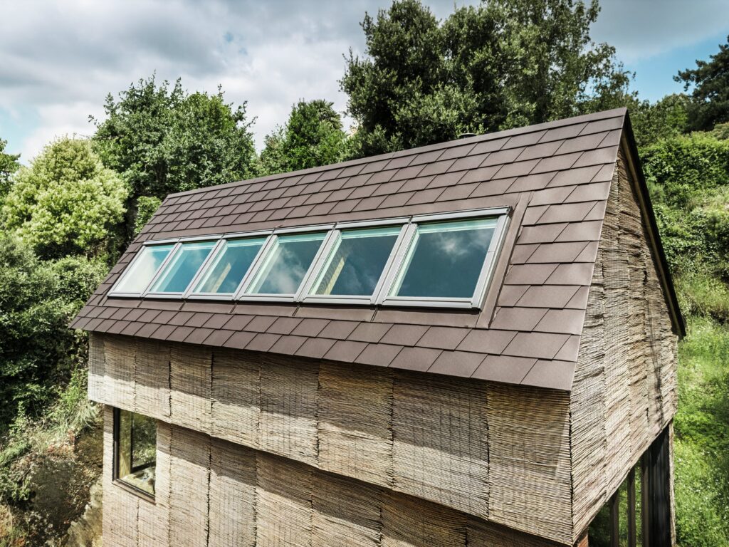 Ein besonderes Detail ist das langgezogene Fensterband, das fast über die gesamte Dachbreite reicht und die Schindeloberfläche unterbricht. © Croce & Wir