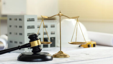 Bauwerkvertragsrechtliche Gegenstände wie ein Richterhammer, eine Waage der Gerechtigkeit, ein Schutzhelm, sowie Baupläne und ein Baumodell liegen auf einem Tisch.