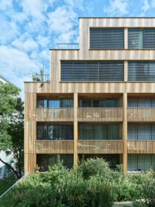 Ein mehrstöckiges Holzhaus mit Balkonen. Die Fassade ist hier näher zu sehen.