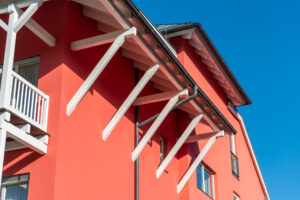 Die hohe Farbtonstabilität von „Evocryl“ sorgt dafür, dass das kräftige Rot selbst bei intensiver Sonneneinstrahlung nicht verblasst. Vor dem Auftragen der Schlussbeschichtung bereitete das Verarbeiterteam die Fassade mit „Rausan KR K2 3516“ und „Lacryl Tiefgrund 595“ vor.© Brillux